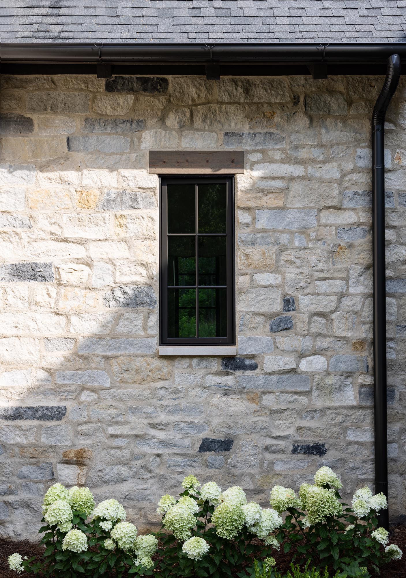 Window in the overgrouted thin stone wall with a cedar header above and a limestone sill below