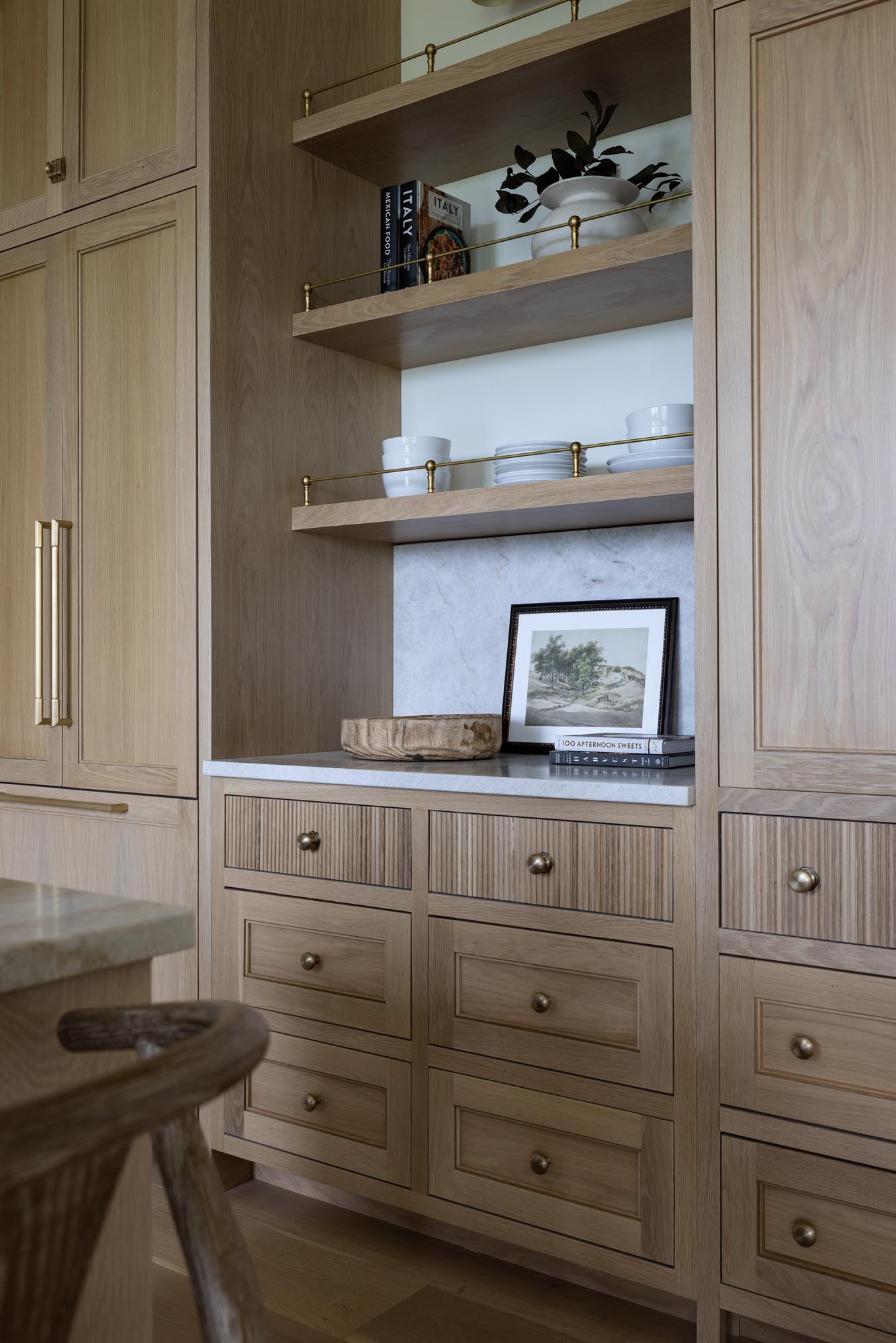 White oak open shelves with brass gallery rails above a Taj Mahal quartzite niche in a white oak kitchen
