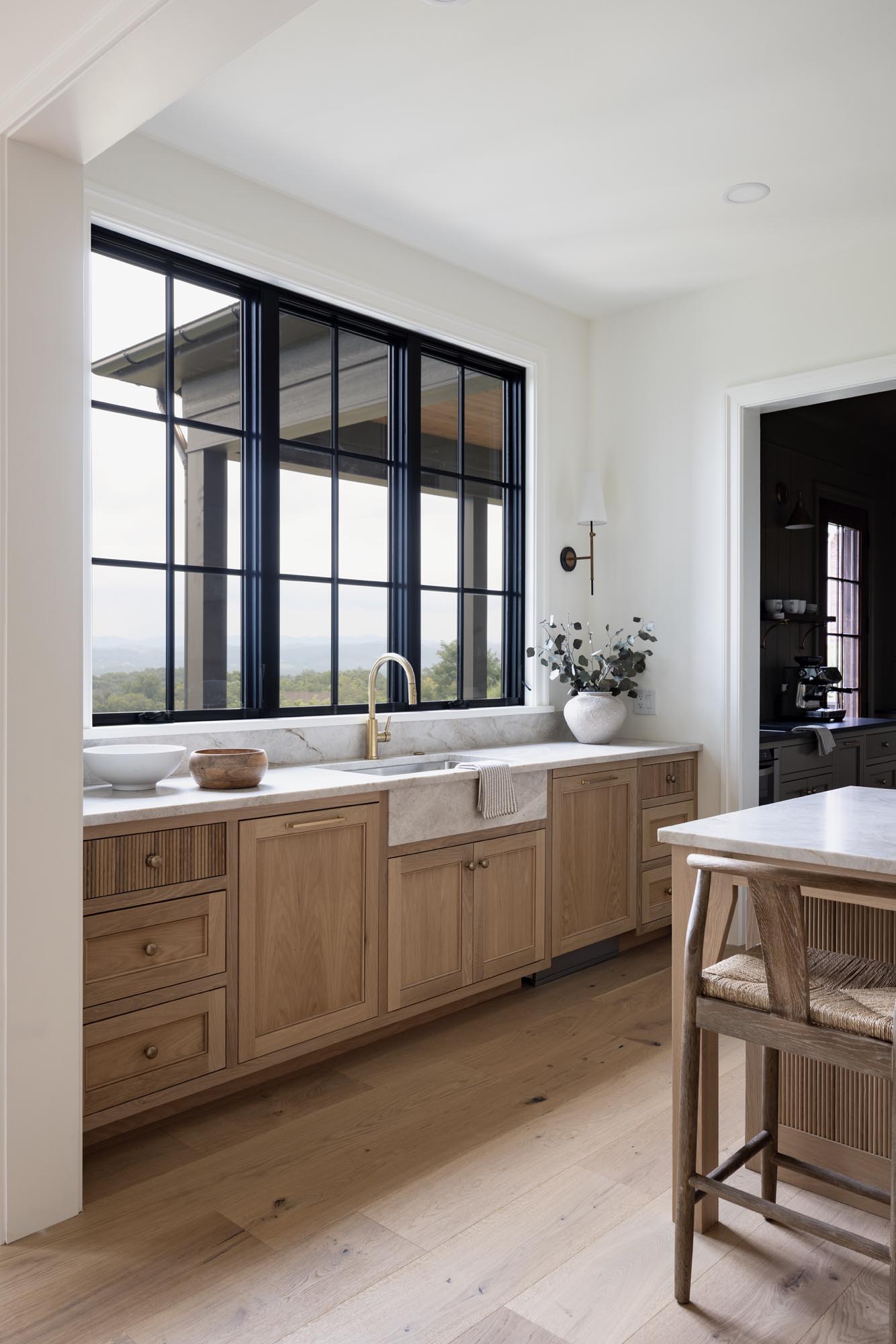 White oak kitchen with inset cabinets, quartzite apron-front sink, brass faucet and black-framed Windsor window
