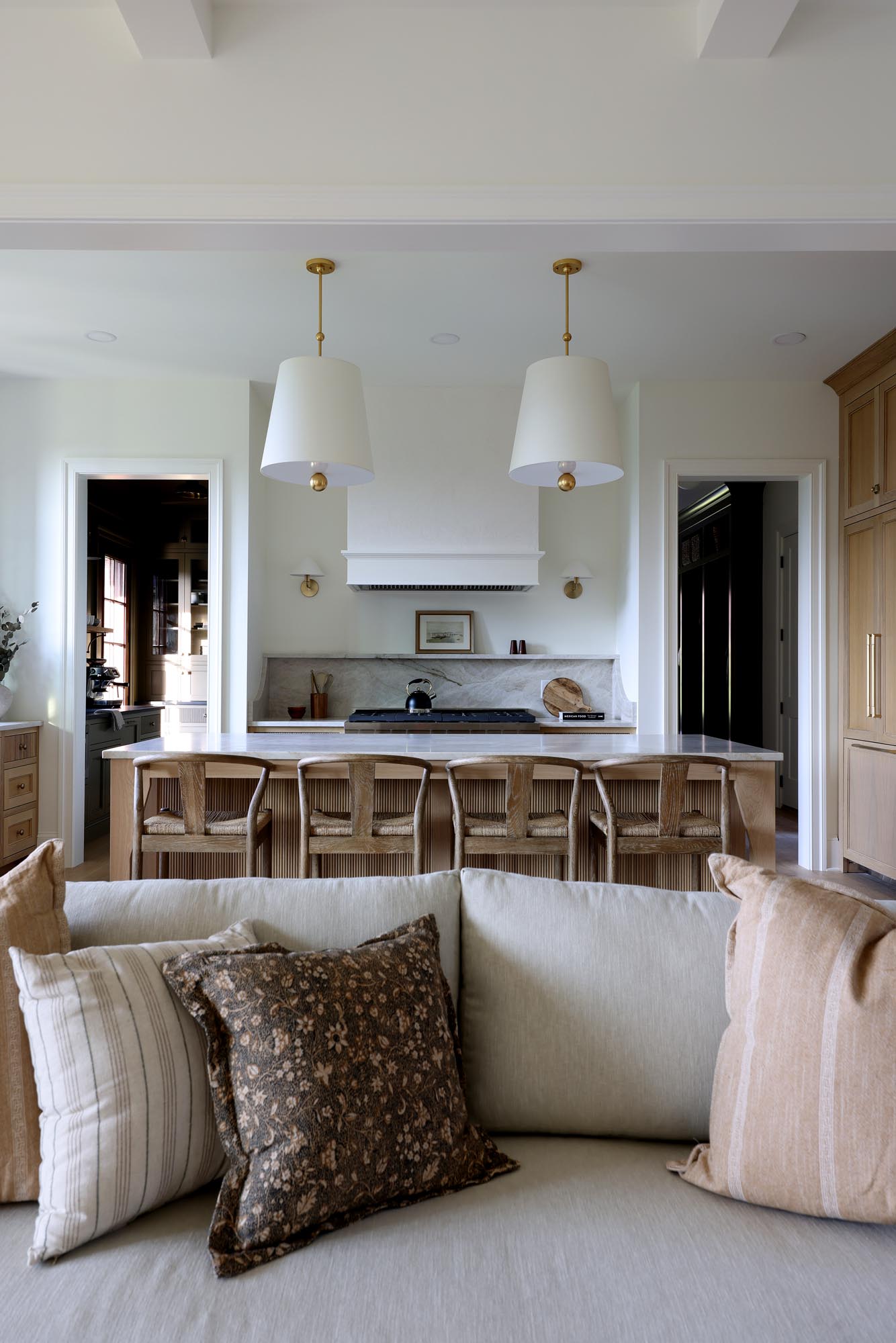 View from the living room to the white oak kitchen island and range with doorways to scullery and mudroom